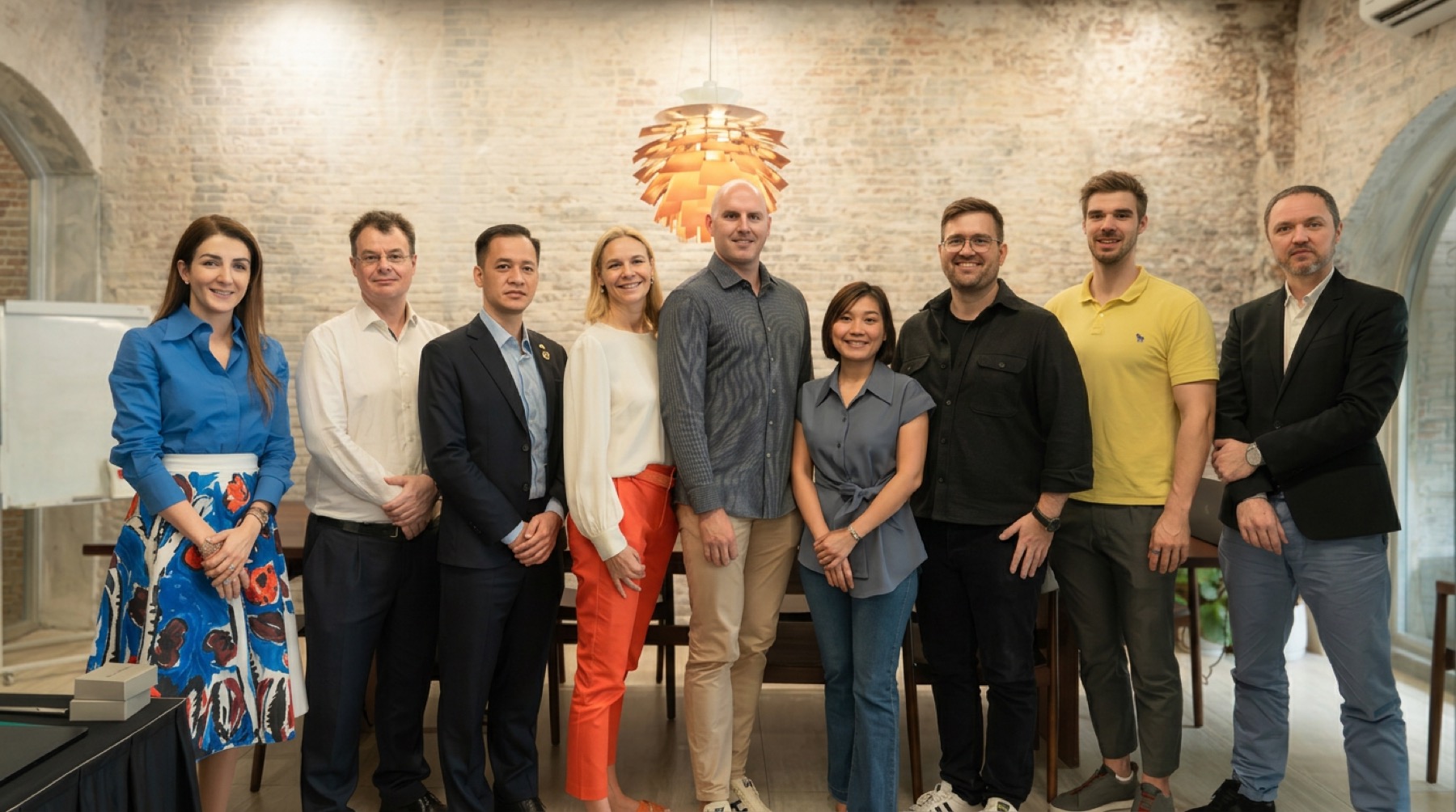 The NordCham Vietnam team standing together under a Danish pendant lamp against a whitewashed brick wall